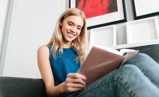 Uśmiechnięta kobieta odpoczywa książkę do czytania i czyta w domu