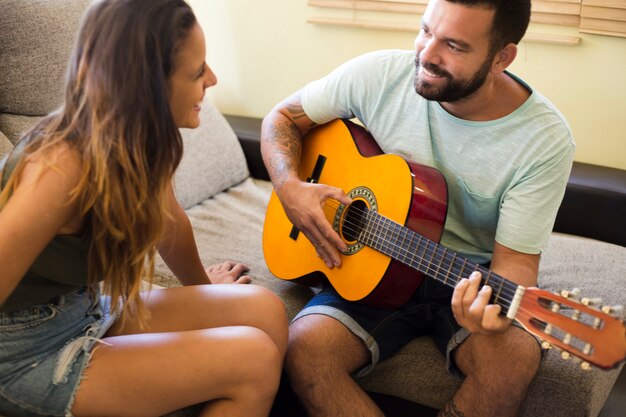 Uśmiechnięta kobieta patrzeje jej męża bawić się gitarę