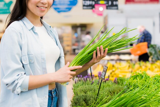 Uśmiechnięta kobieta podnosi zieleni w sklepie spożywczym