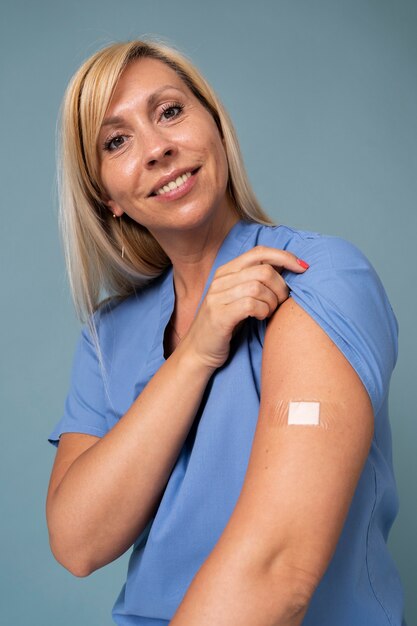 Uśmiechnięta kobieta pokazująca ramię z naklejką po otrzymaniu szczepionki