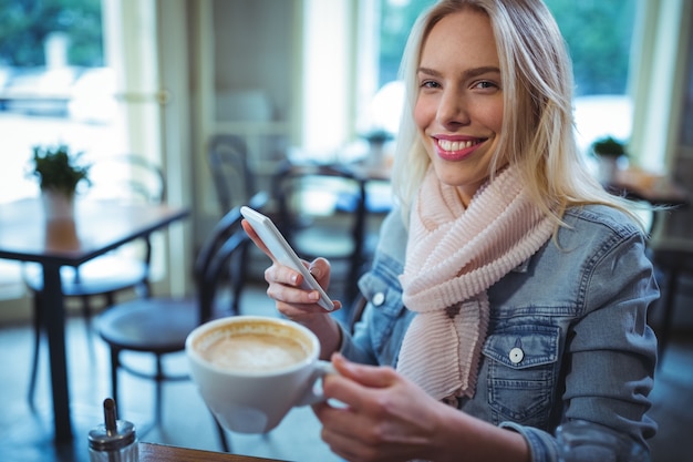 Uśmiechnięta kobieta przy użyciu telefonu komórkowego w Caf