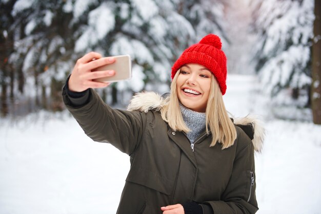 Uśmiechnięta kobieta robi selfie w zimowym lesie