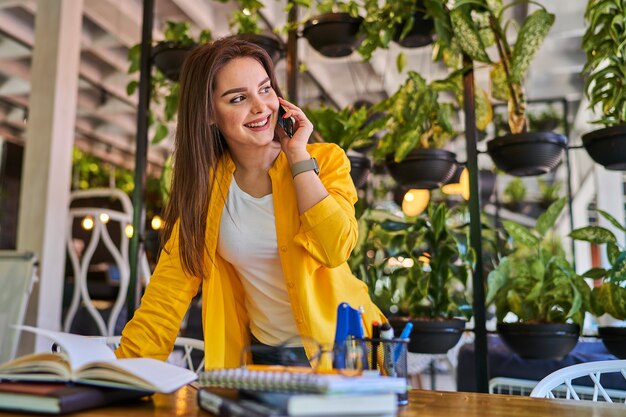 Uśmiechnięta kobieta rozmawia przez telefon komórkowy w swoim biurze.