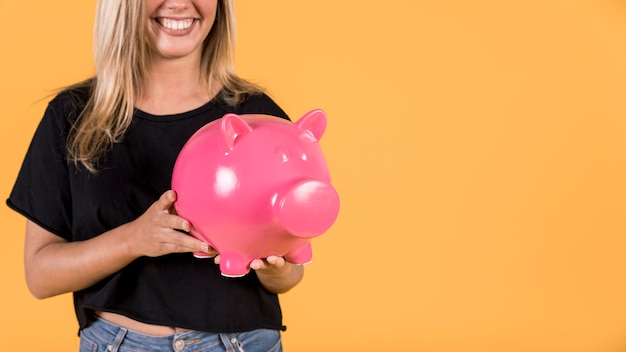 Uśmiechnięta kobieta trzyma różowego prosiątko banka przeciw jaskrawemu tłu