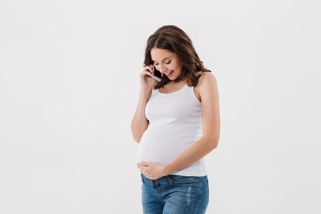 Uśmiechnięta kobieta w ciąży rozmawia przez telefon komórkowy