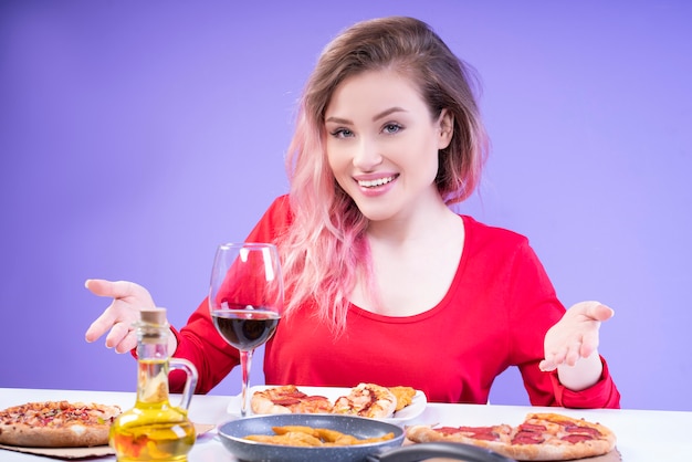 Uśmiechnięta kobieta w czerwonej bluzce i różowych włosach zaprasza na obiad