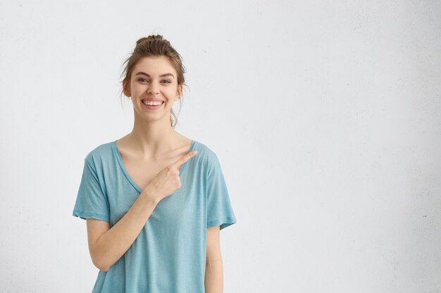uśmiechnięta kobieta w niebieskiej koszuli, wskazując na pustą białą ścianę, pokazując coś