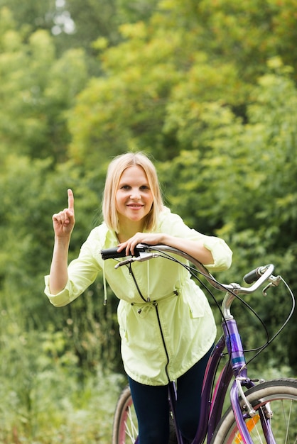 Bezpłatne zdjęcie uśmiechnięta kobieta wskazuje up na bicyklu