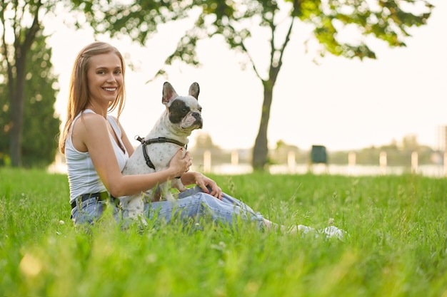 Uśmiechnięta kobieta z buldogiem francuskim na trawie