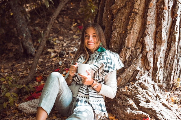 Uśmiechnięta kobieta z napojem w lesie