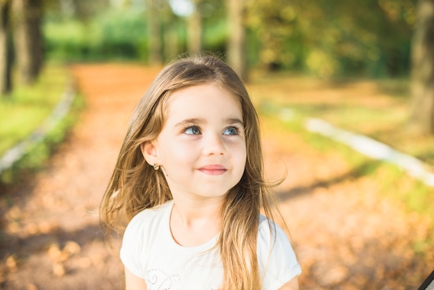 Uśmiechnięta mała dziewczynka w parku patrzeje daleko od