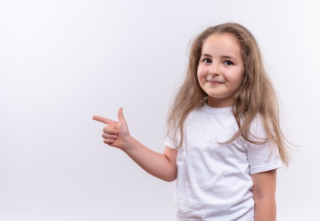 Uśmiechnięta mała uczennica ubrana w biały t-shirt punkty z boku na na białym tle