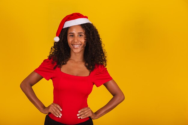 Uśmiechnięta młoda african american kobieta w boże narodzenie kapelusz na białym tle na żółtym tle ściany, portret studio. koncepcja wakacje obchody szczęśliwego nowego roku 2021. makieta miejsca na kopię