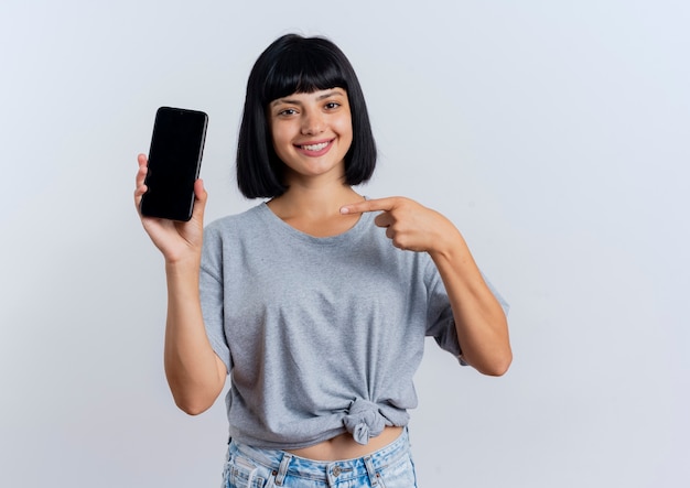 Uśmiechnięta młoda brunetka dziewczynka kaukaski trzyma i wskazuje na telefon