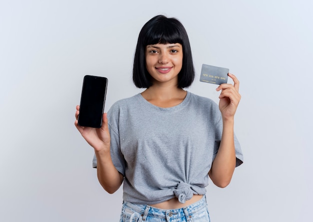 Uśmiechnięta młoda brunetka kaukaska kobieta trzyma telefon i kartę kredytową