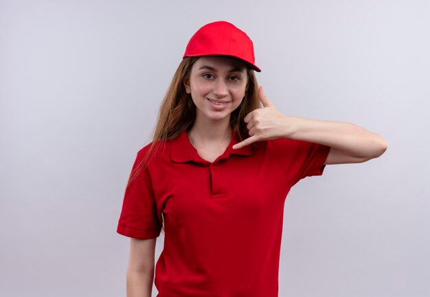 Uśmiechnięta młoda dziewczyna dostawy robi gest połączenia w czerwonym mundurze na na białym tle białej przestrzeni z miejsca na kopię