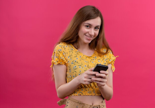 Uśmiechnięta młoda dziewczyna trzyma telefon komórkowy i patrząc na na białym tle różową ścianę z miejsca na kopię