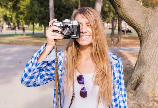 Bezpłatne zdjęcie uśmiechnięta młoda kobieta bierze fotografię na kamerze przy outdoors