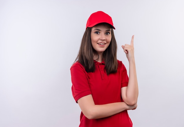 Uśmiechnięta młoda kobieta dostawy ubrana w czerwoną koszulkę w czerwonej czapce wskazuje na pojedyncze białe ściany