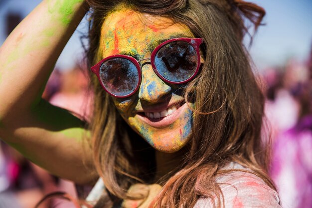 Uśmiechnięta młoda kobieta jest ubranym okulary przeciwsłonecznych z holi proszkiem na jej twarzy