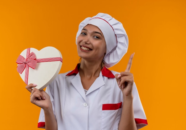 Uśmiechnięta Młoda Kobieta Kucharz Ubrana W Mundur Szefa Kuchni Trzymając Serce W Kształcie Wskazuje Palcem Na Pole Na Na Białym Tle Pomarańczowy