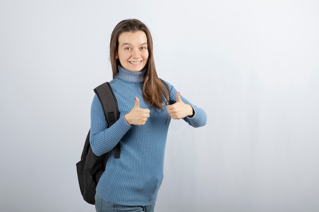 uśmiechnięta młoda kobieta model z plecakiem pokazując kciuk do góry.