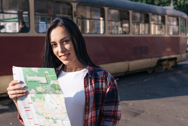 Uśmiechnięta młoda kobieta patrzeje kamerę podczas gdy trzymający mapę