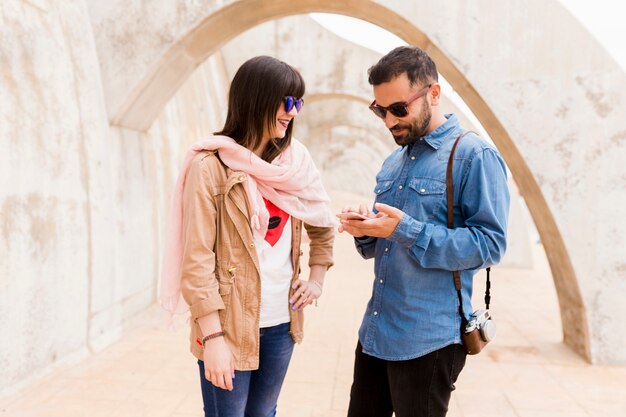 Bezpłatne zdjęcie uśmiechnięta młoda kobieta patrzeje mężczyzna używa telefon komórkowego