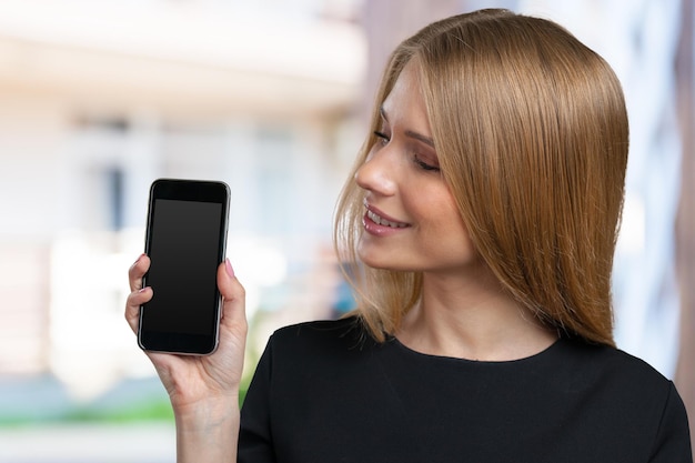 Uśmiechnięta młoda kobieta pokazująca pusty ekran smartfona