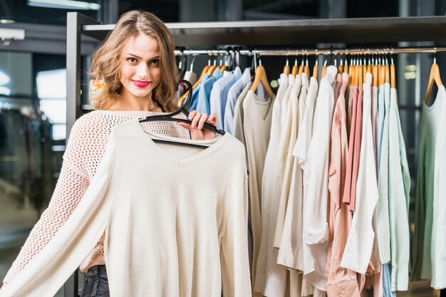 Uśmiechnięta młoda kobieta próbuje na nowe ubrania w sklepie odzieżowym