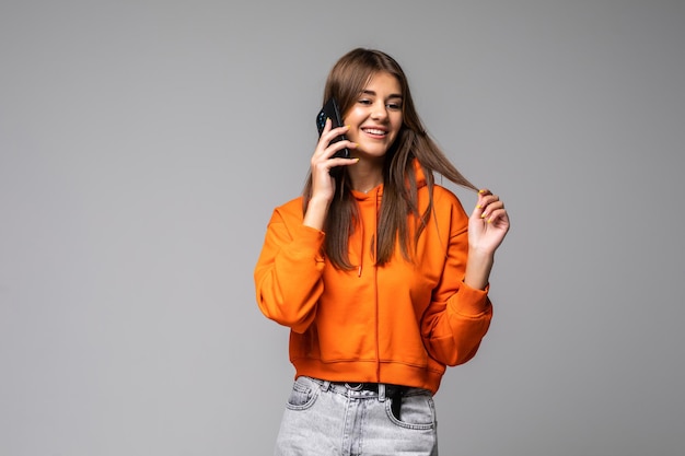 Uśmiechnięta młoda kobieta rozmawiająca przez smartfona na szarym tle