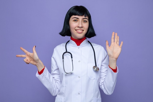 Uśmiechnięta młoda ładna kaukaska dziewczyna w mundurze lekarza ze stetoskopem wskazującym osiem palcami