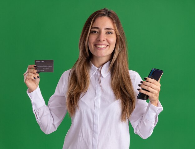 Uśmiechnięta młoda ładna kaukaski dziewczyna trzyma kartę kredytową i telefon na zielono
