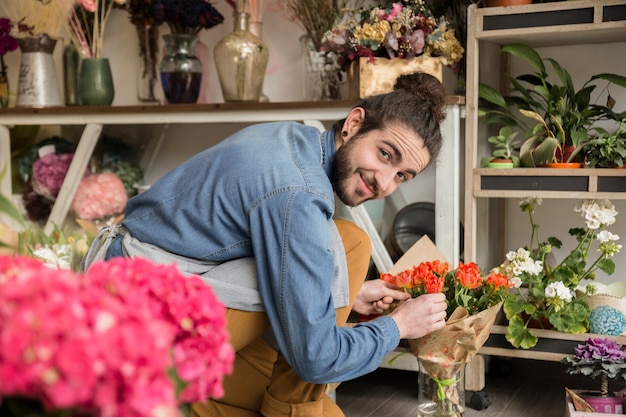 Bezpłatne zdjęcie uśmiechnięta młoda męska kwiaciarnia układa kwiatu w bukiecie
