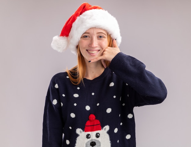 Bezpłatne zdjęcie uśmiechnięta młoda piękna dziewczyna w świątecznym kapeluszu pokazującym gest połączenia telefonicznego na białej ścianie