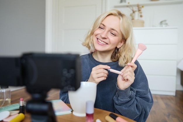 Uśmiechnięta, młoda, piękna, lifestyle bloggerka nagrywa vlog o pięknie w swoim pokoju, używając profesjonalnych