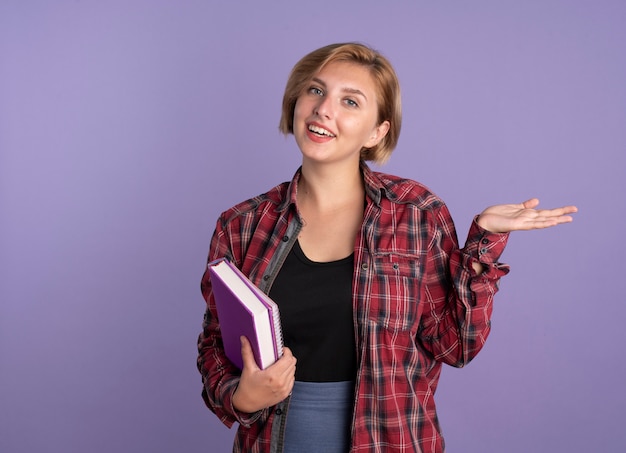 Uśmiechnięta młoda słowiańska studentka trzyma książkę, a notatnik trzyma rękę otwartą