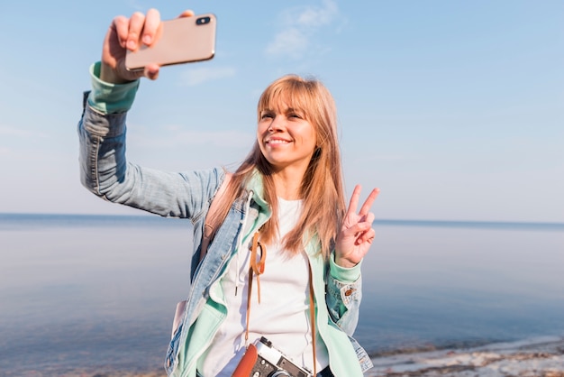 Uśmiechnięta młodej kobiety pozycja przed morzem bierze selfie na smartphone