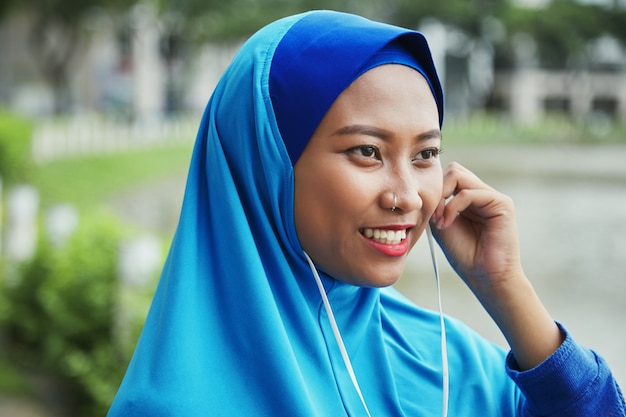 Uśmiechnięta Muzułmańska kobieta czopuje słuchawki na ulicie