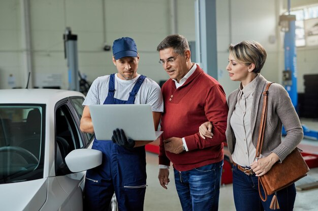 Uśmiechnięta para i ich mechanik korzystający z laptopa w warsztacie