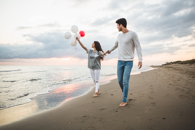 Bezpłatne zdjęcie uśmiechnięta para spaceru na plaży z balonów