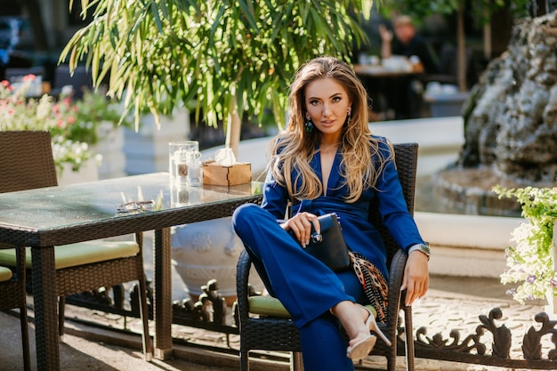 Uśmiechnięta piękna kobieta ubrana w elegancki niebieski garnitur siedzi w kawiarni w słoneczny jesienny dzień