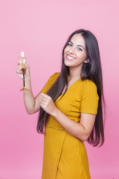 Uśmiechnięta piękna młoda kobieta trzyma szampańskiego flet przeciw różowemu tłu