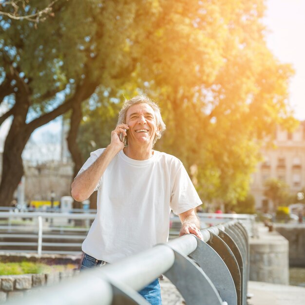 Uśmiechnięta starszego mężczyzna pozycja w parku opowiada na telefonie komórkowym