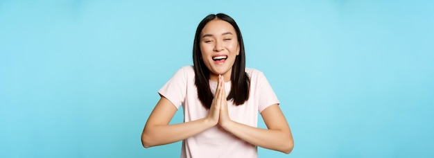Uśmiechnięta szczęśliwa azjatycka kobieta pokazuje namaste błagalny gest i marzy o czymś, co budzi wielkie nadzieje