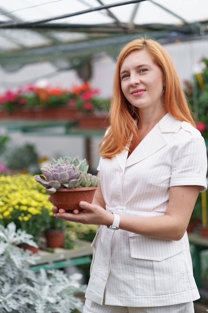 Uśmiechnięta Szczęśliwa Kwiaciarka W Swoim Przedszkolu Stojąca, Trzymając W Rękach Doniczkową Kombinację Sukulentów, Gdy Zajmuje Się Roślinami Ogrodowymi W Szklarni