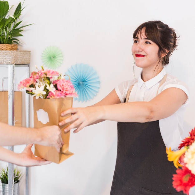 Uśmiechnięta żeńska kwiaciarnia daje kwiat papierowej torbie jej klient