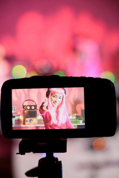 Bezpłatne zdjęcie uśmiechnięty artysta grający piosenkę elektroniczną na konsoli miksera podczas nagrywania sesji muzycznej przy użyciu profesjonalnej kamery, przygotowujący się do występu w nocnym klubie. dj z różowymi włosami kręci wideo z jej występem