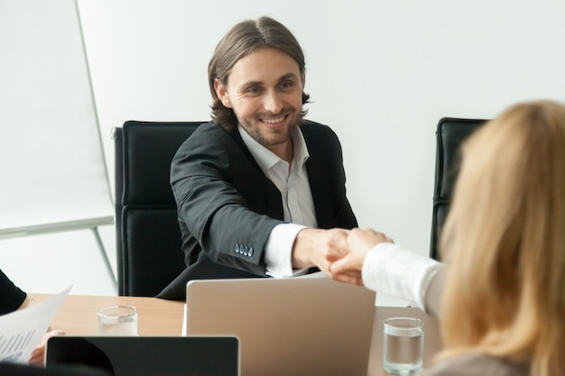 Uśmiechnięty biznesmen w kostiumu handshaking żeńskim partnerze przy grupowym spotkaniem