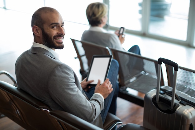 Bezpłatne zdjęcie uśmiechnięty biznesmen za pomocą cyfrowego tabletu w poczekalni